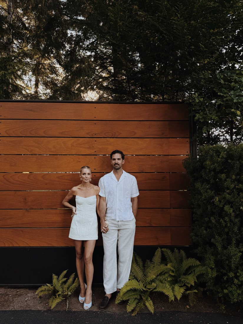 Katie and Danny in white, standing against a slatted wood wall